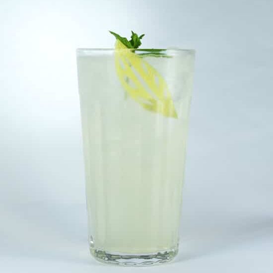 Elderflower sling cocktail in a tall glass with ice and a garnish of mint and carved lemon peel.